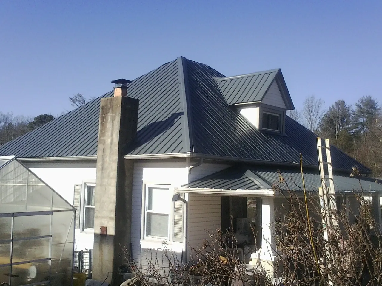 Dark blue standing seam metal roof on a white farmhouse with dormer — Slate & Tile Roof Repair by Roofing Brothers in North Judson