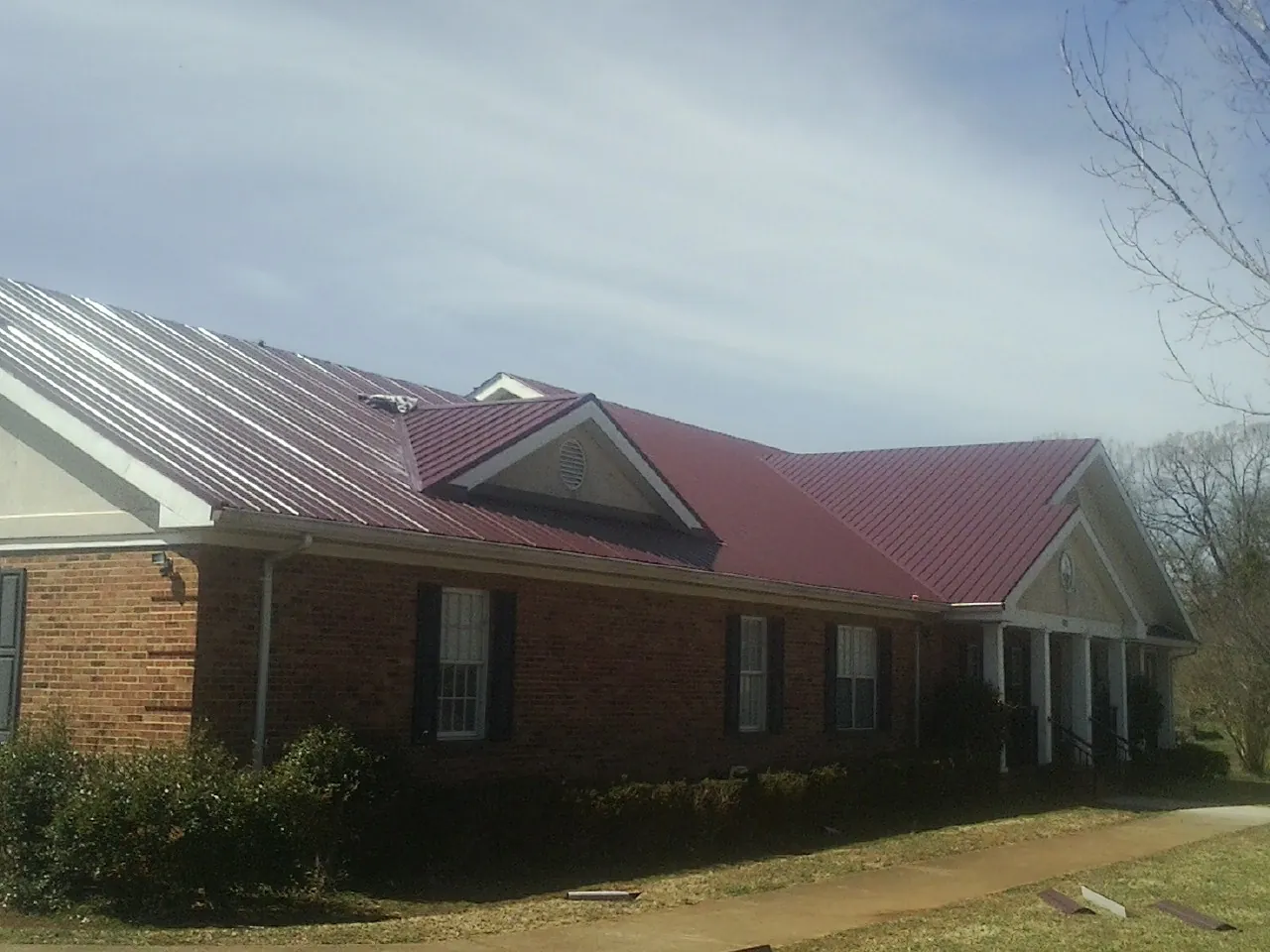 Red metal roof with gabled entries on a long brick building, from a Hail Damage Roof Repair job in North Judson