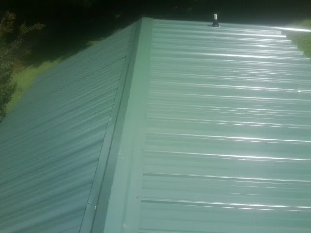 New green metal panels meeting at the ridge of a roof — Flat Roof Repair work by our crew in North Judson