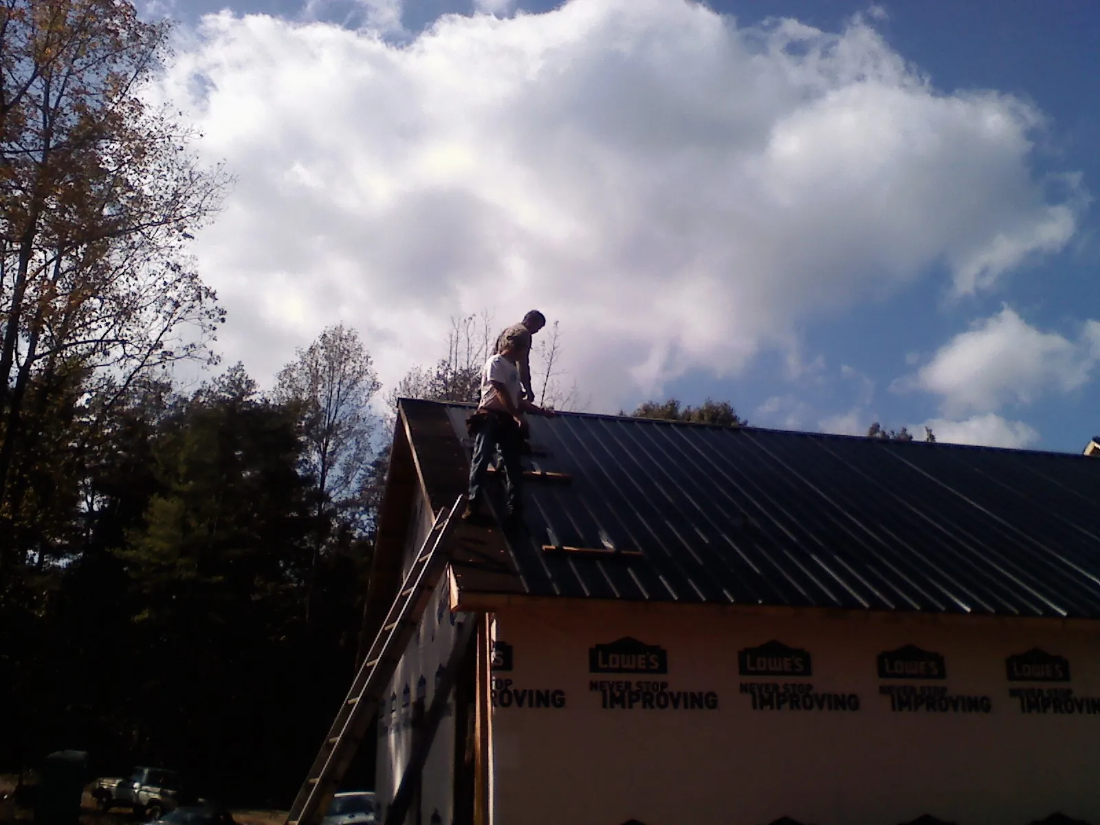 Roofer fastening dark metal panels high against a cloudy sky, from a Roof Inspection job in North Judson