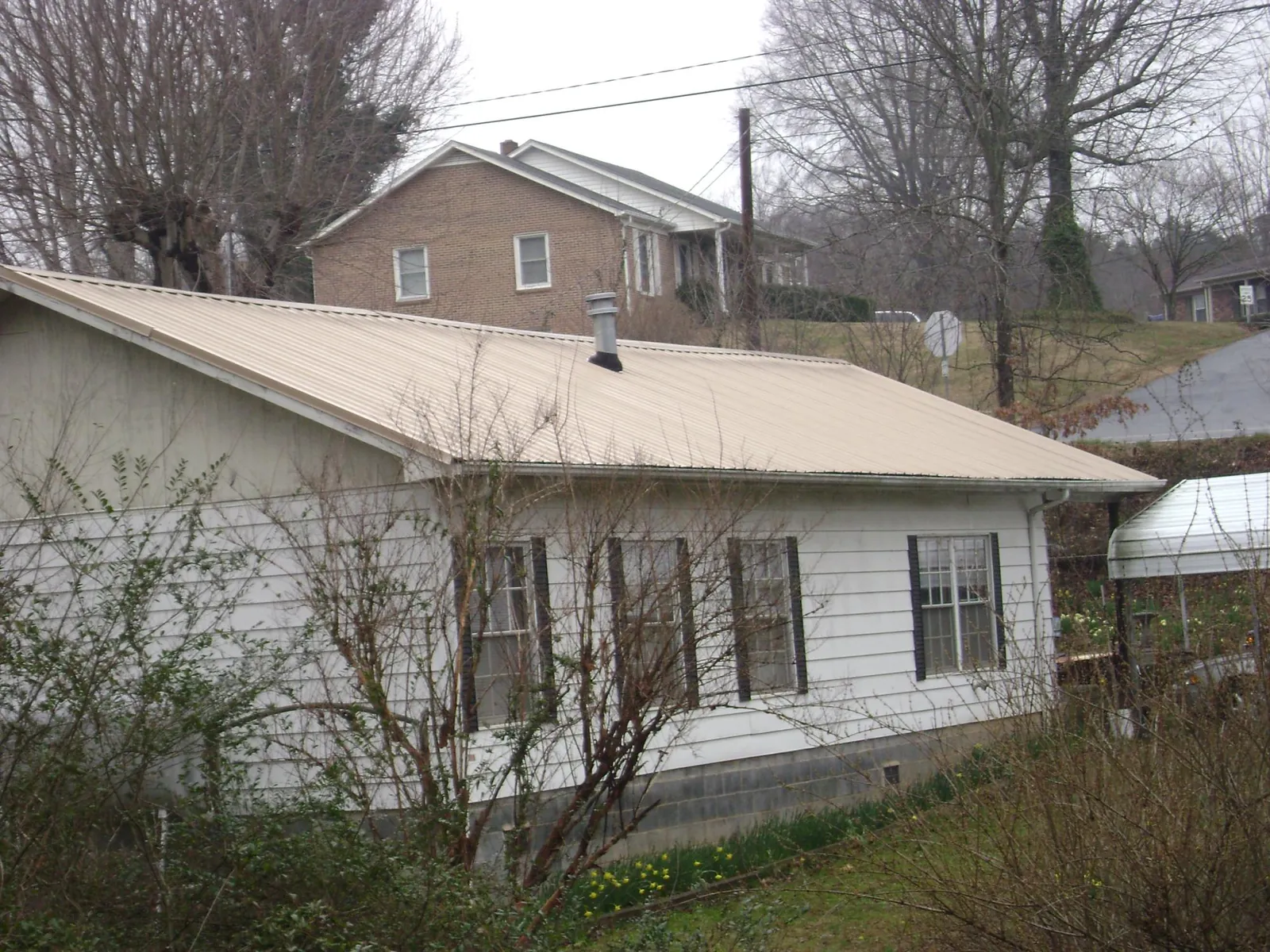 Tan metal roof on a white sided house set into a hillside — Commercial Roofing by Roofing Brothers in North Judson